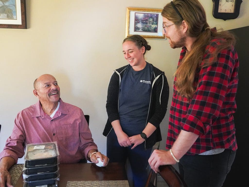 Two volunteers chatting with a Meals on Wheels senior recipient.