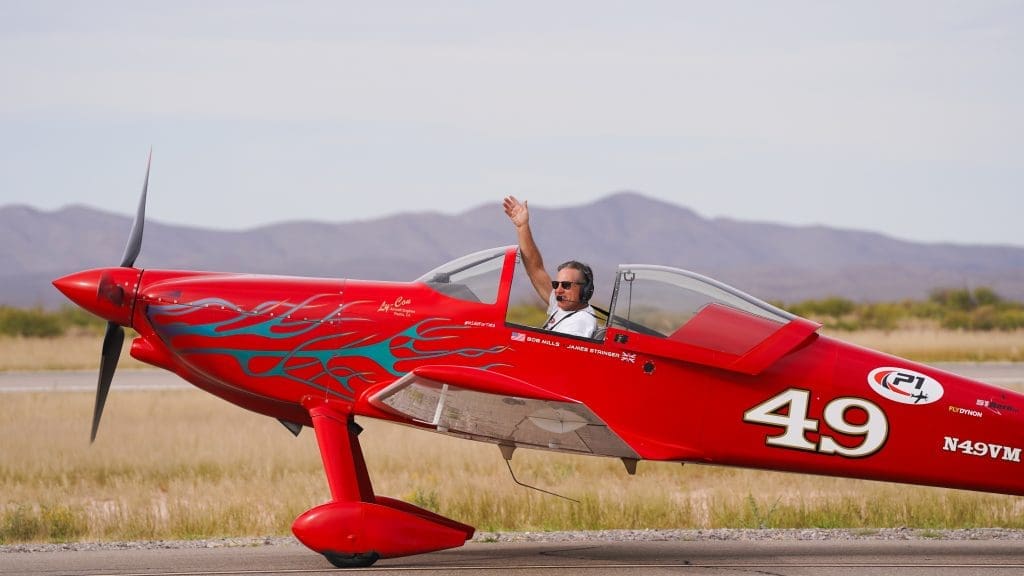 A pilot waves from a small red airplane.