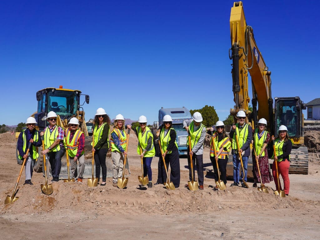 A group of people lined up with hard hats and construction vests with shovels at a construction site.