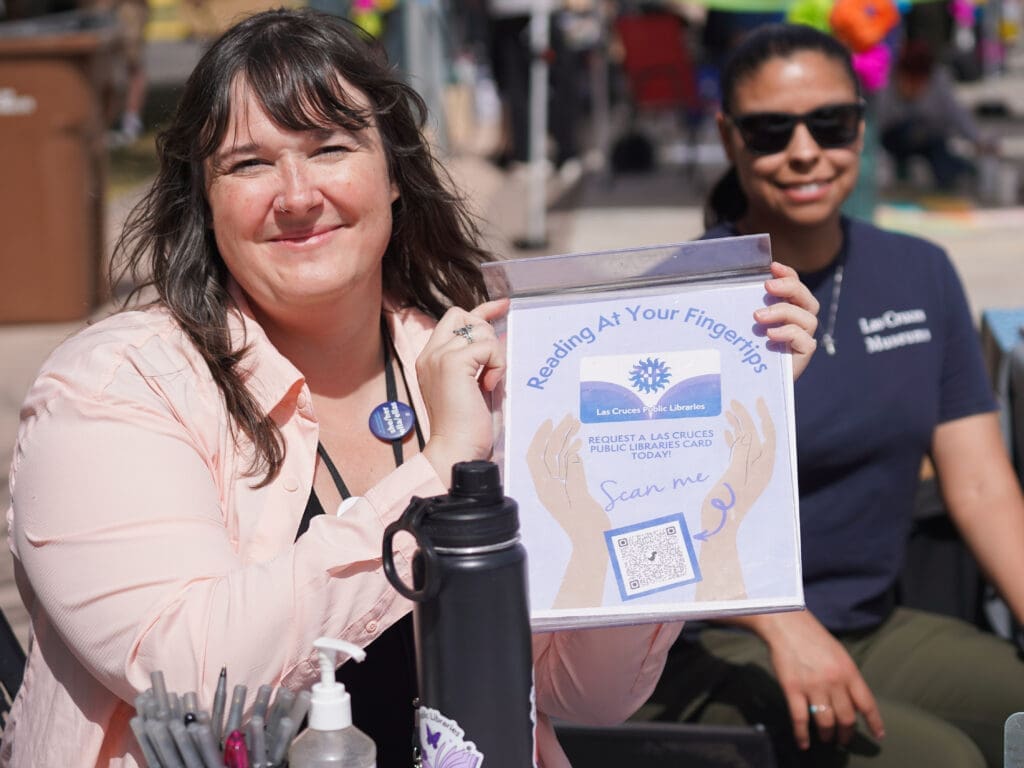 A woman holds a sign with information on how to register for a library card.