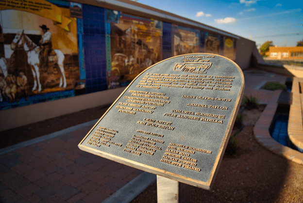 Photo of dedication plaque with tiled mural in background.