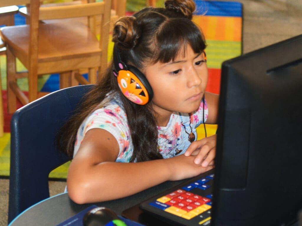 A child wears headphones while they sit in front of a computer.