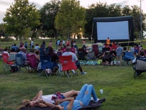 People in park in front of an inflatable movie screen on the grass.