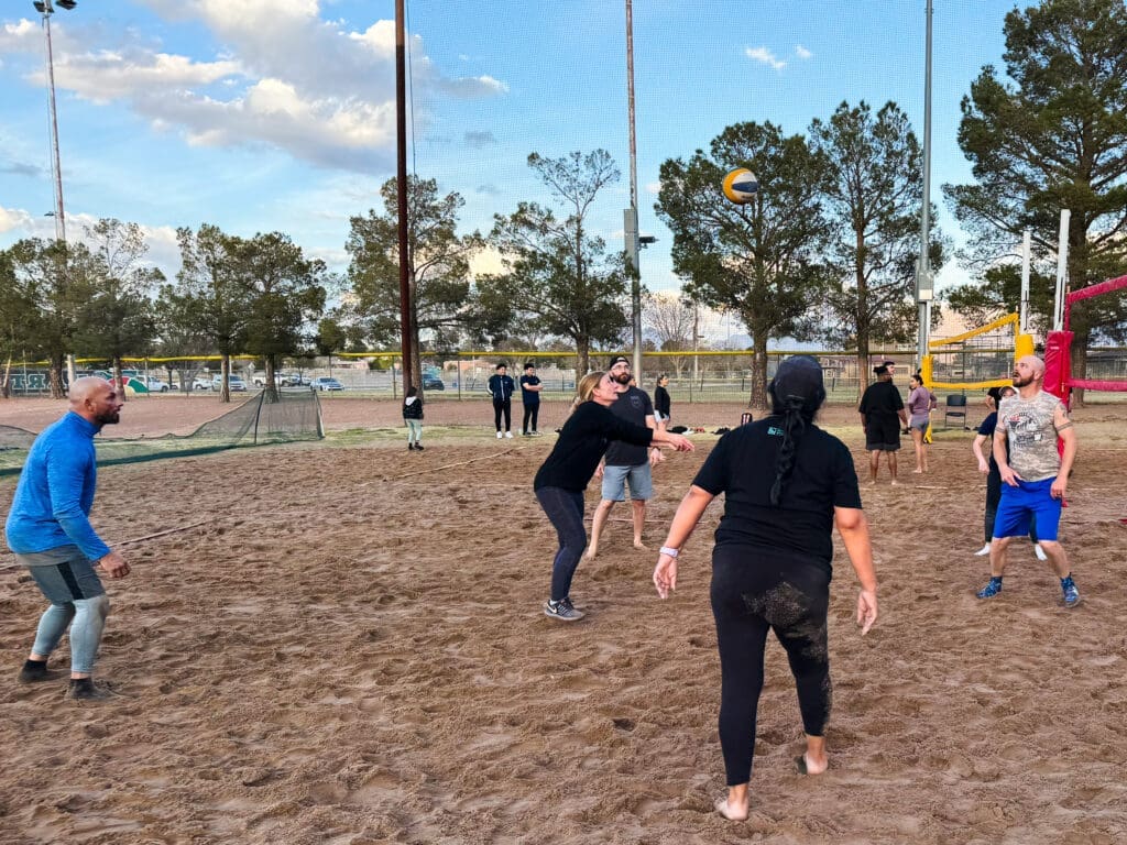 A group of adults play volleyball in a sand.