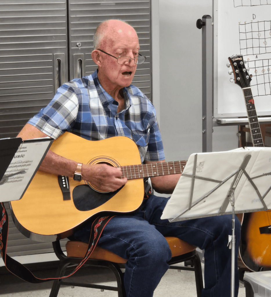 Senior male playing guitar and singing at Eastside community center