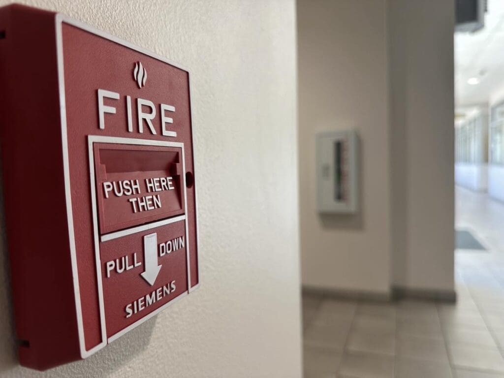 Fire Pull Alarm with extinguisher and hallway in background.