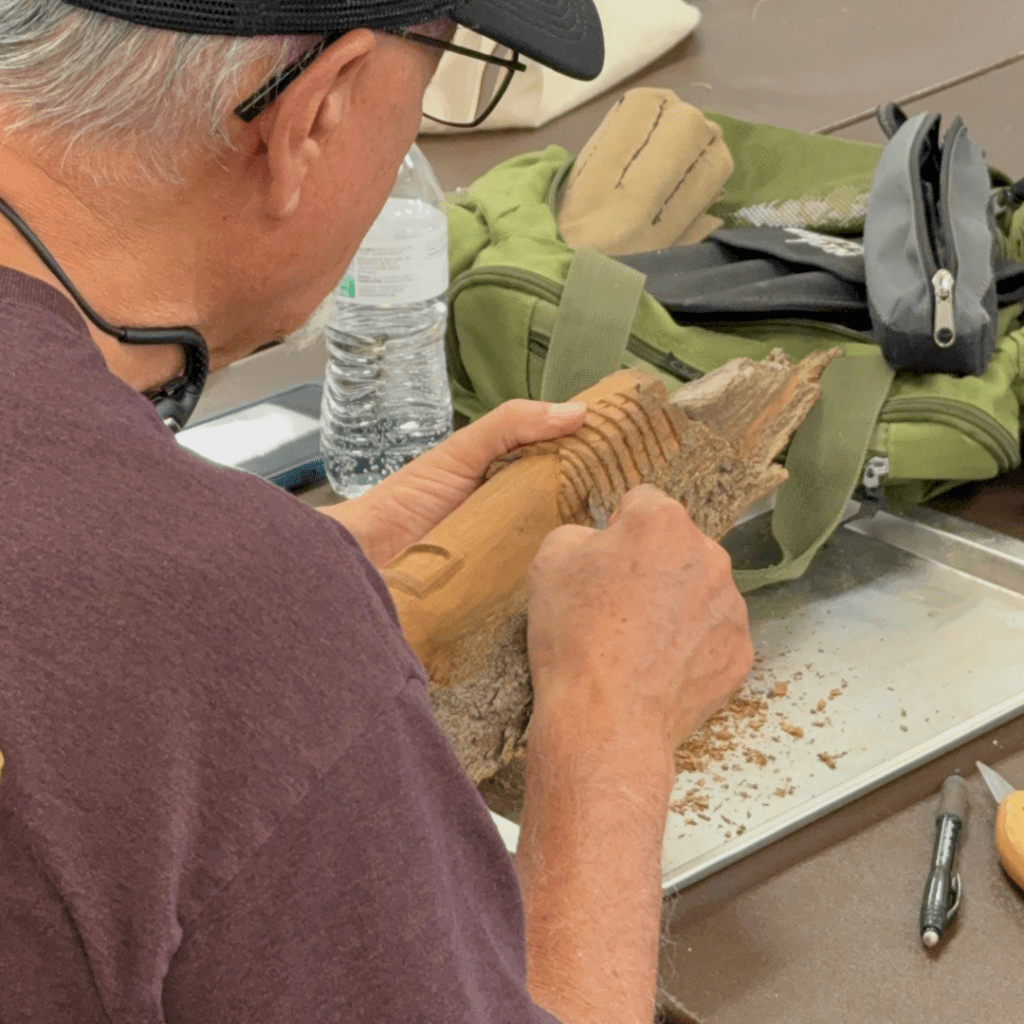 Senior male carving a piece of wood with hand tools