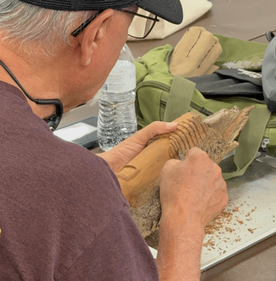 Senior male carving a piece of wood with hand tools