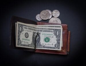 wallet with folded bills inside and change spilling out from it on a table.