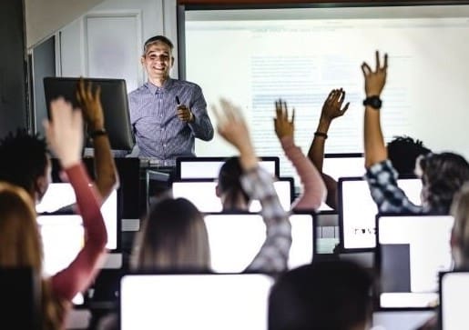 Students raising hands at a computer class