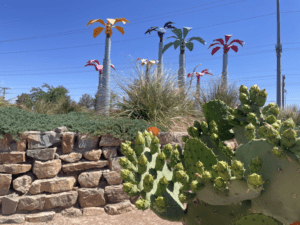 Metal palm tree sculpture behind rock wall and cactus