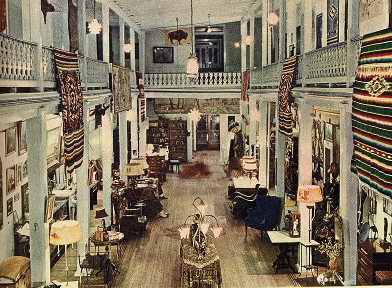 Image from 1946 showing the period for interior restoration of the Amador Hotel. There are rugs hung from the second floor draping down the railing and lots of ornate furniture.