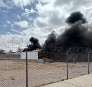 Two firefighters fighting fire with heavy smoke coming out of the building.