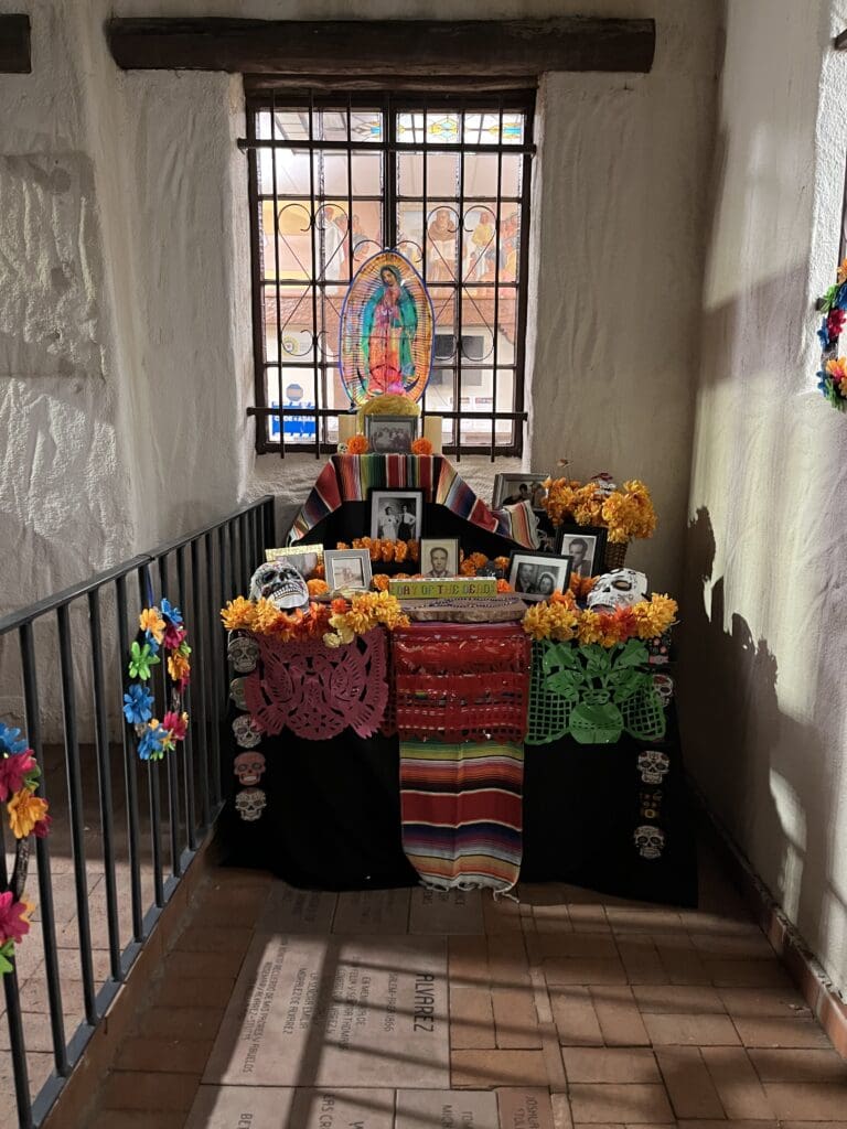 An altar in front of the Branigan Cultural Center with picturees and a stained glass Our Lady of Guadalupe at the top.