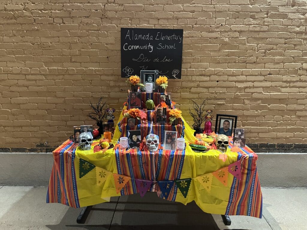 An altar from Alameda community school with three tiers featuring skulls and pictures.