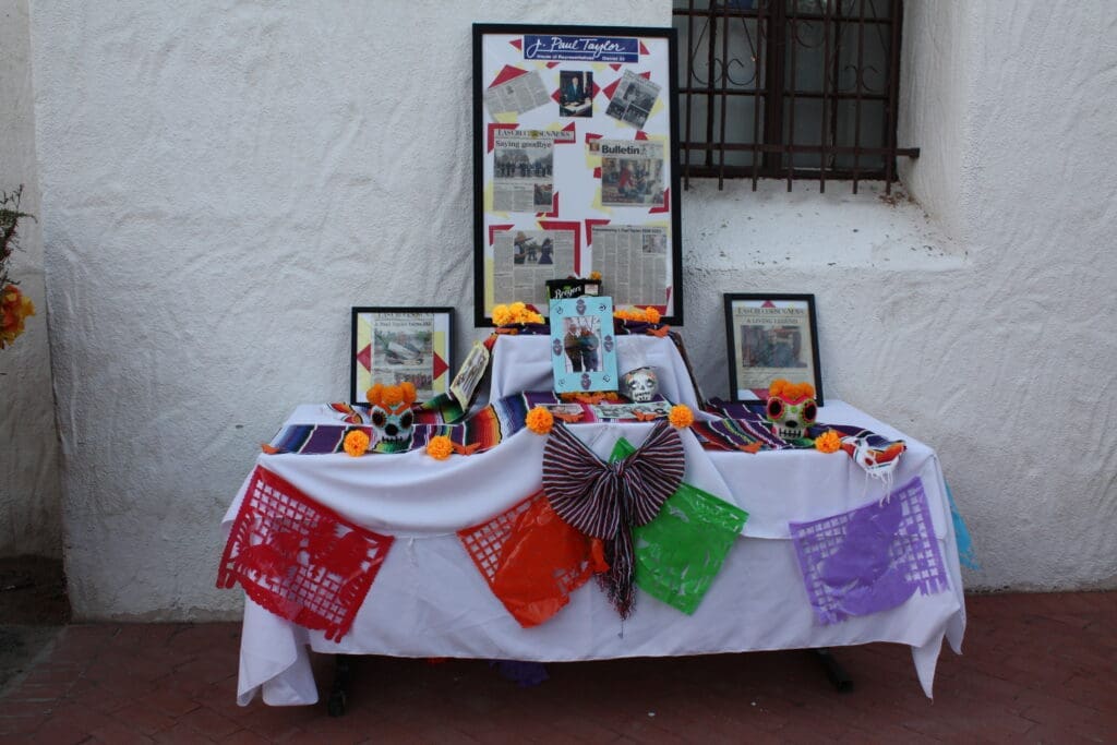 A community altar from J. Paul Taylor Academy with a large board with pictures and articles. The altar has papel picado banners and marigolds on it.