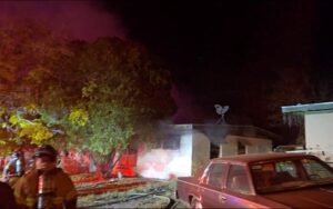 House with smoke coming out of windows with fire crew in front of it.