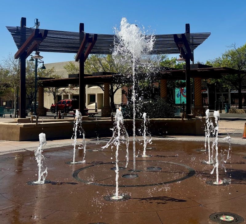 A fountain with water coming up from the ground with a building in the background.