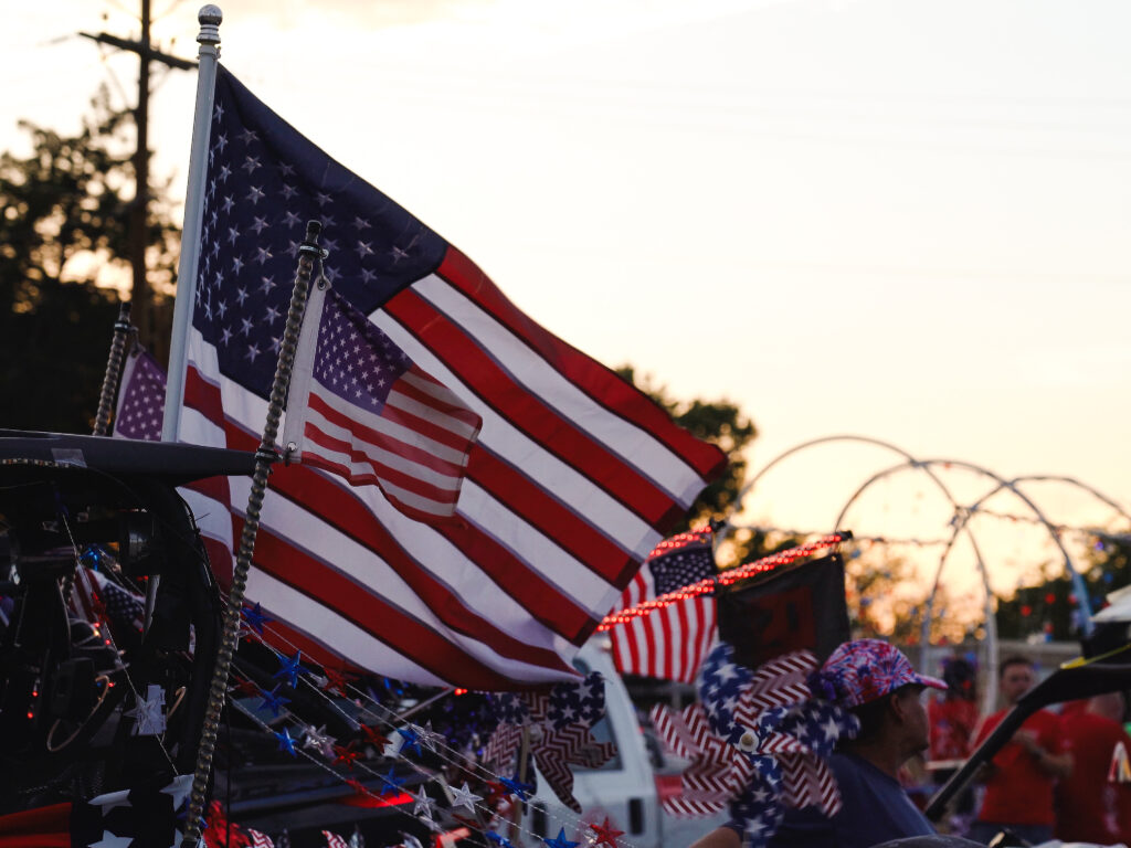 American Flags wave in the air attached to a vehicle during sunset.