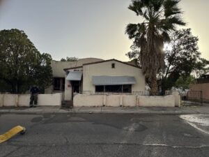 Front of a house with a firefighter standing by the fence.