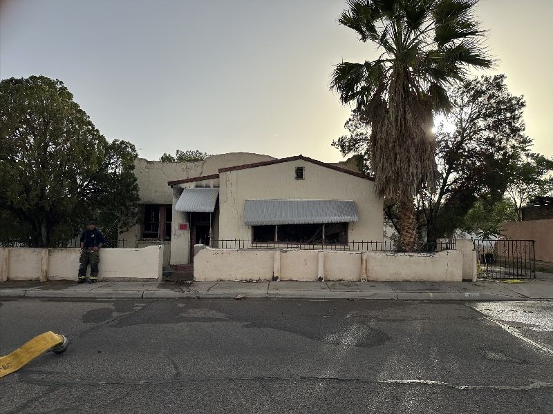 Front of a house with a firefighter standing by the fence.