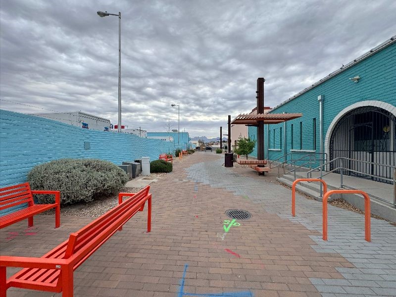 Brick road with red benches between a blue building and a blue wall.