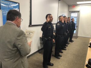 Six police officers in a line with their right hand raised while a man reads something.