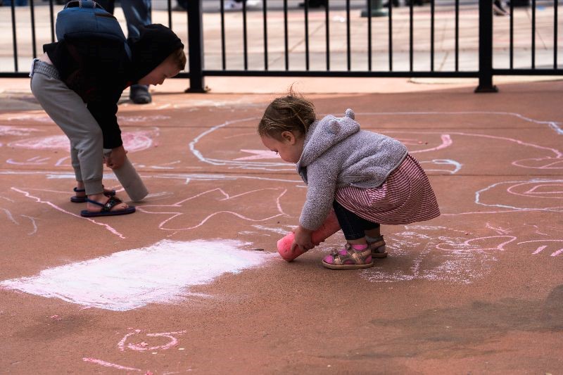 Two children drawing with chalk on the ground.