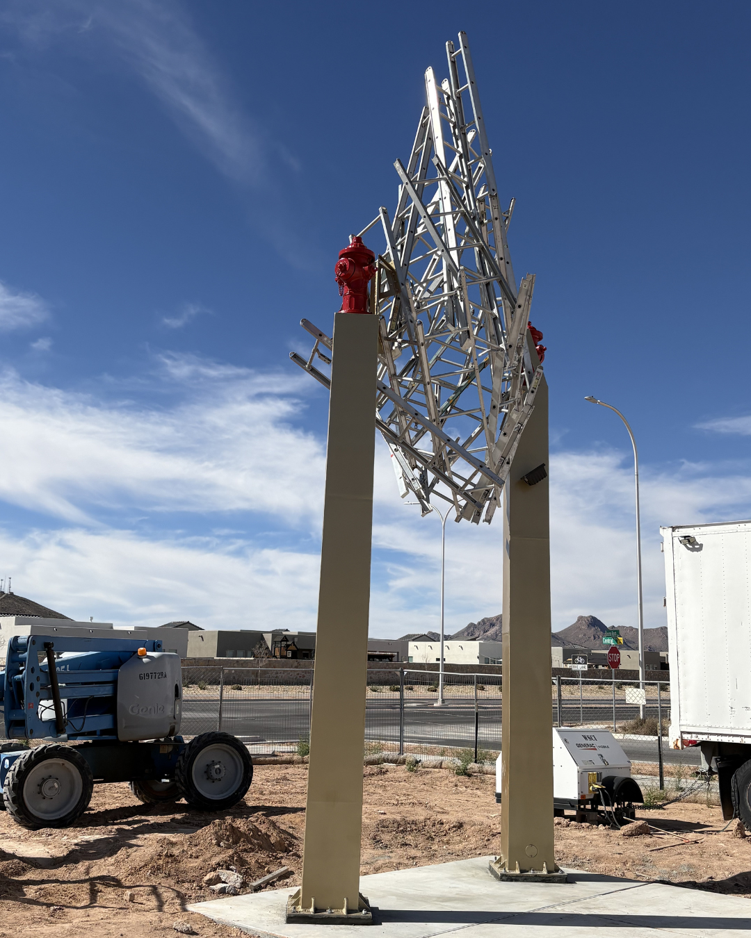steel columns topped with fire hydrants holding spiky ball made of ladders.
