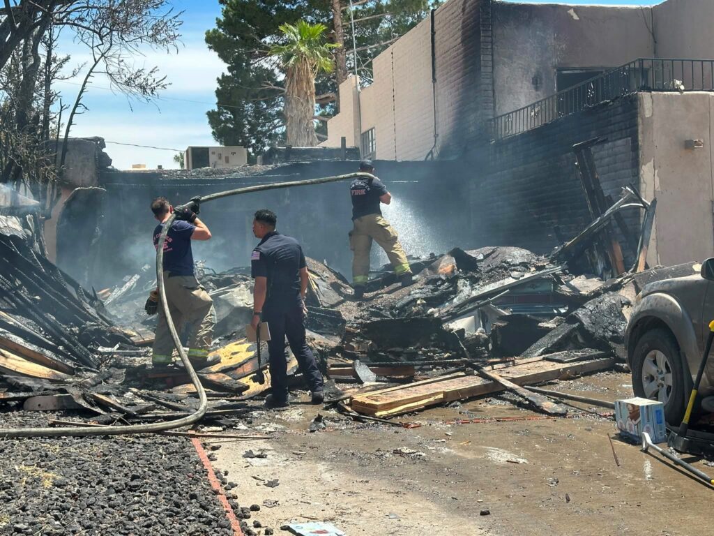 Three firefighters looking through the debris of a house fire.