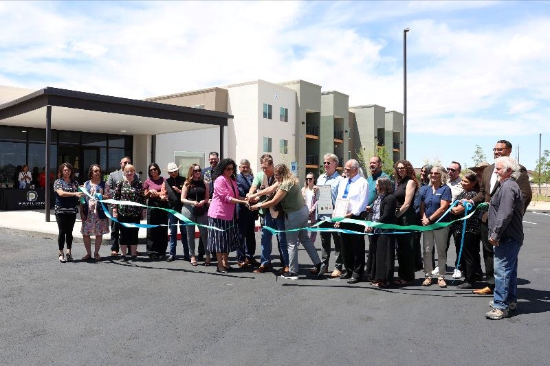 Group of people cutting a ribbon in front of an apartment building.