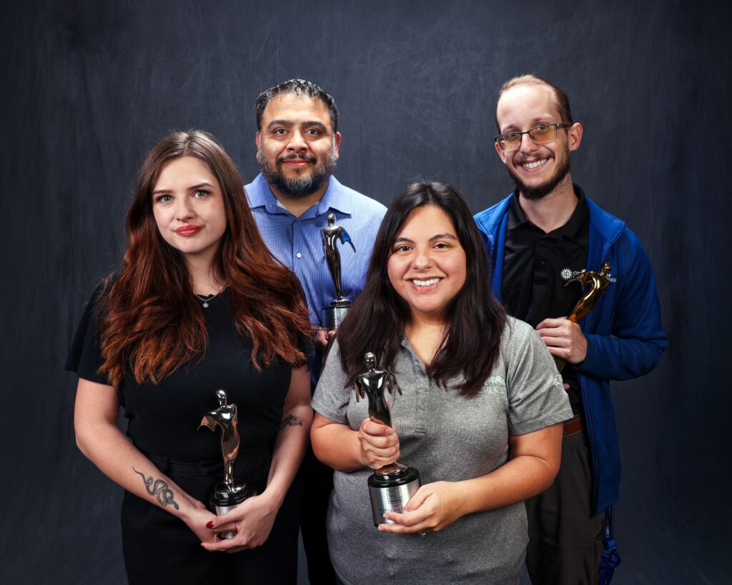 Four people standing while holding trophies.