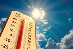 Analog thermometer with the sky and sun in the background.