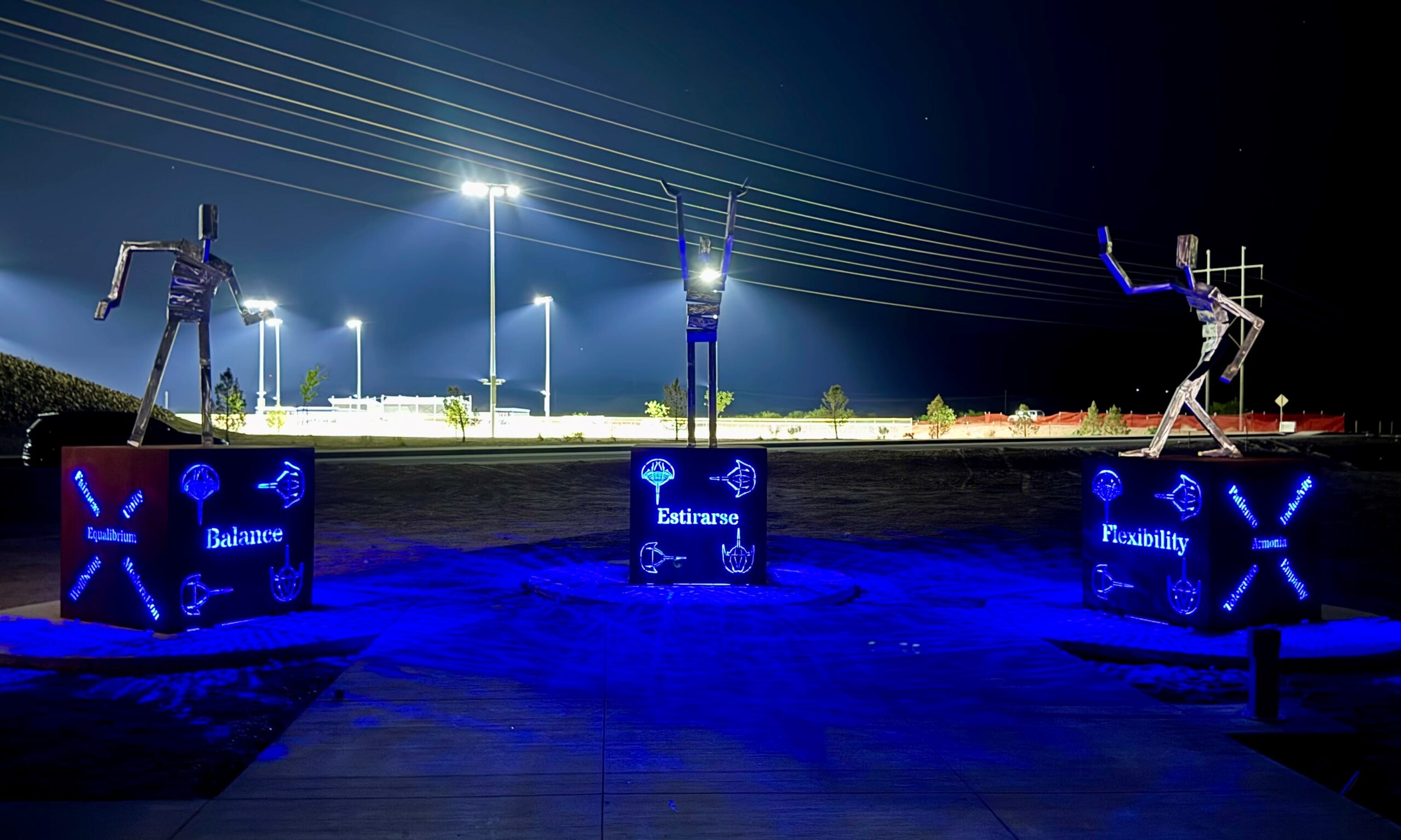 Stylized figures standing on platforms with blue lights shining through cutouts at nighttime.