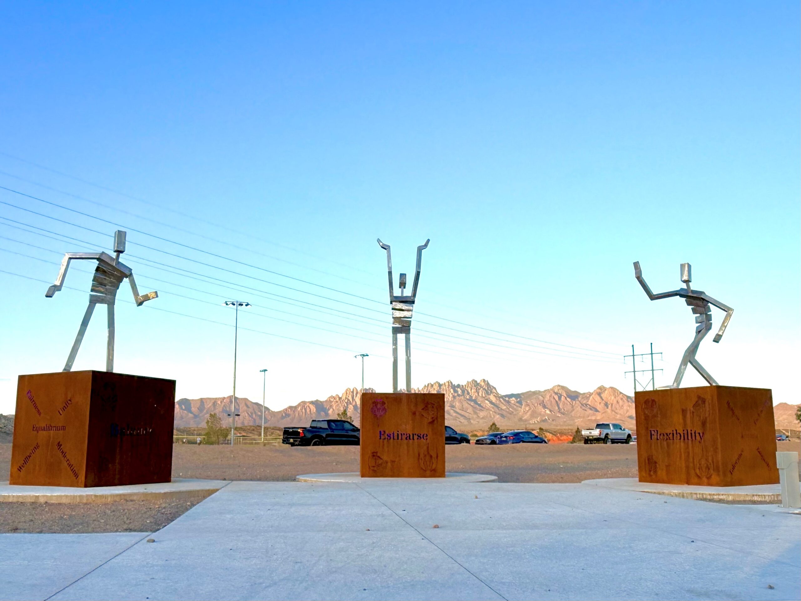 Stylized figures standing on blocks against a backdrop of the Organ Mountains.