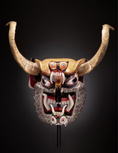 A picture of a mask with large horns and a wide mouth open and full of fangs.