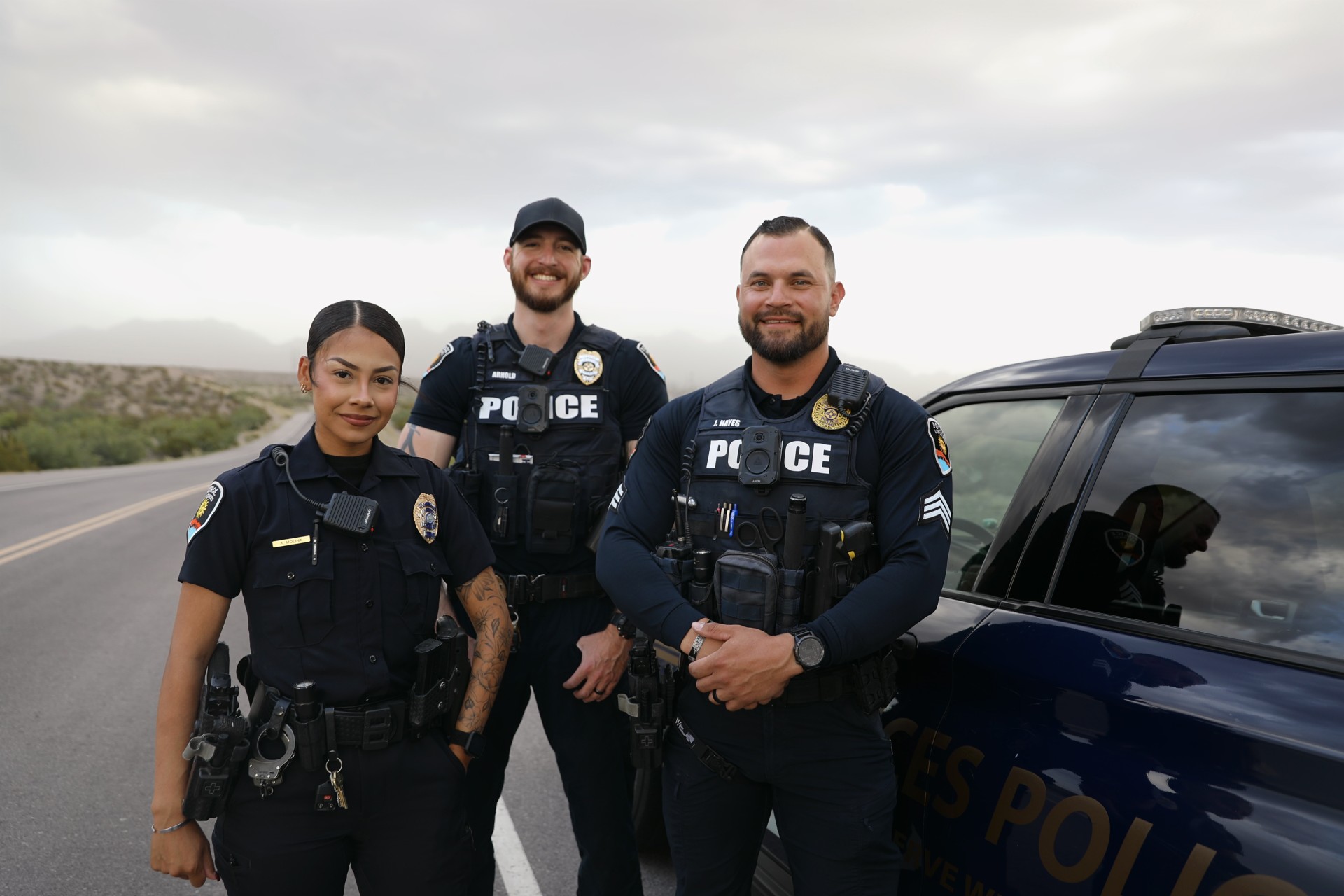 Group of three LCPD officers standing in front of a cruiser, smiling at the camera.