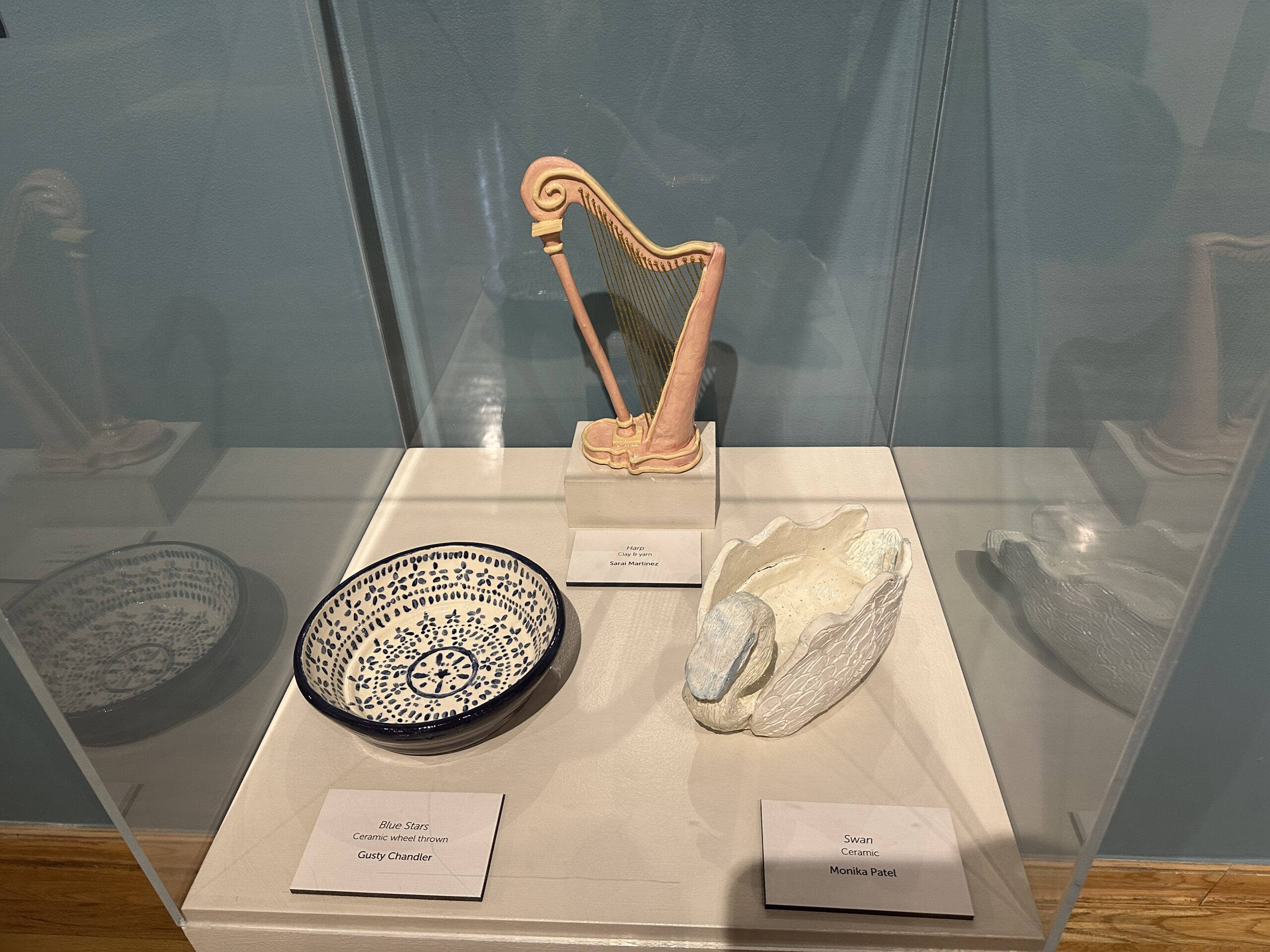 A picture of various ceramic art pieces in a case. One is shaped like a harp, another a bowl, and the third a swan dish.