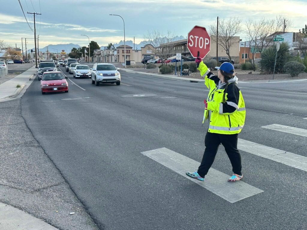 A crossing guard at a crosswalk stopping oncoming traffic.