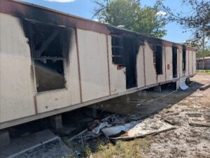 The side of a mobile home with heavy fire damage.