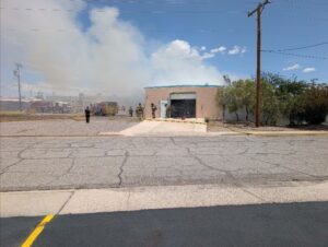 Firefighters standing around a storage building with smoke coming from behind.