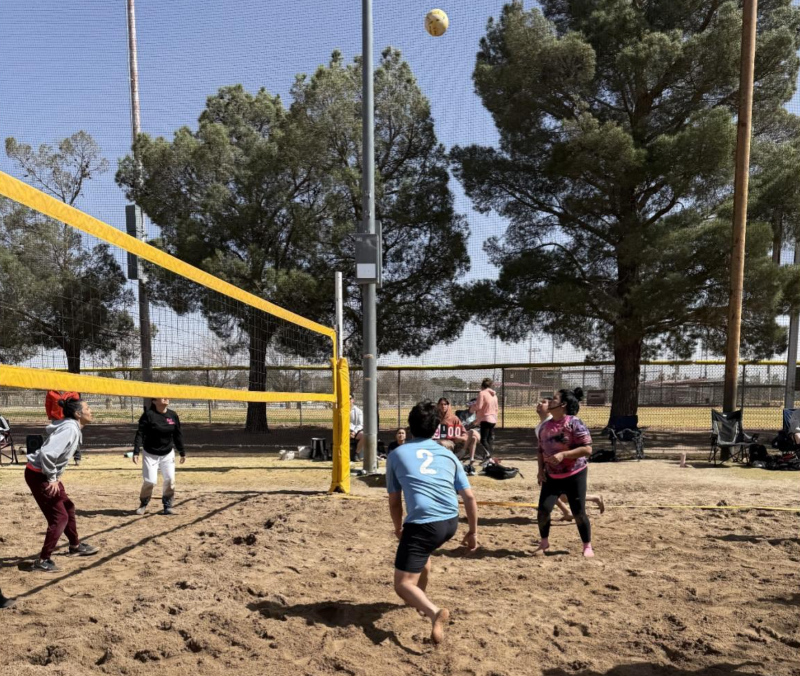 People playing volleyball outside in the sand.