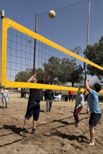 People playing volleyball outside in the sand.