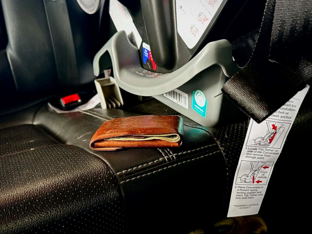 Wallet on the seat of a vehicle next to a car seat.