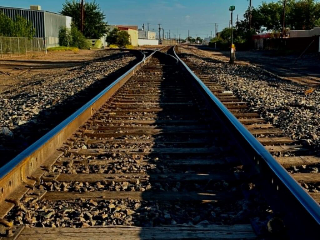 Train tracks with buildings and trees on both sides.