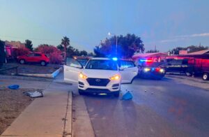A white sedan in the road with its doors open and a police vehicle with its lights on parked in the road also.