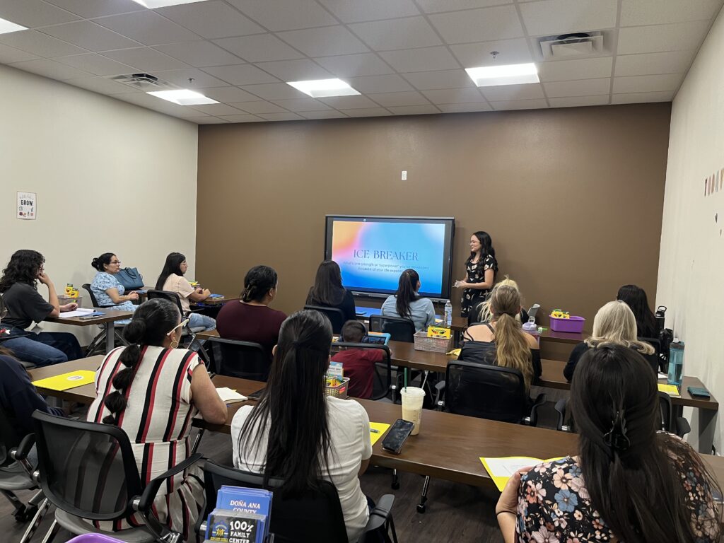 Group of people in a classroom setting with a person at the front of the room near a television.