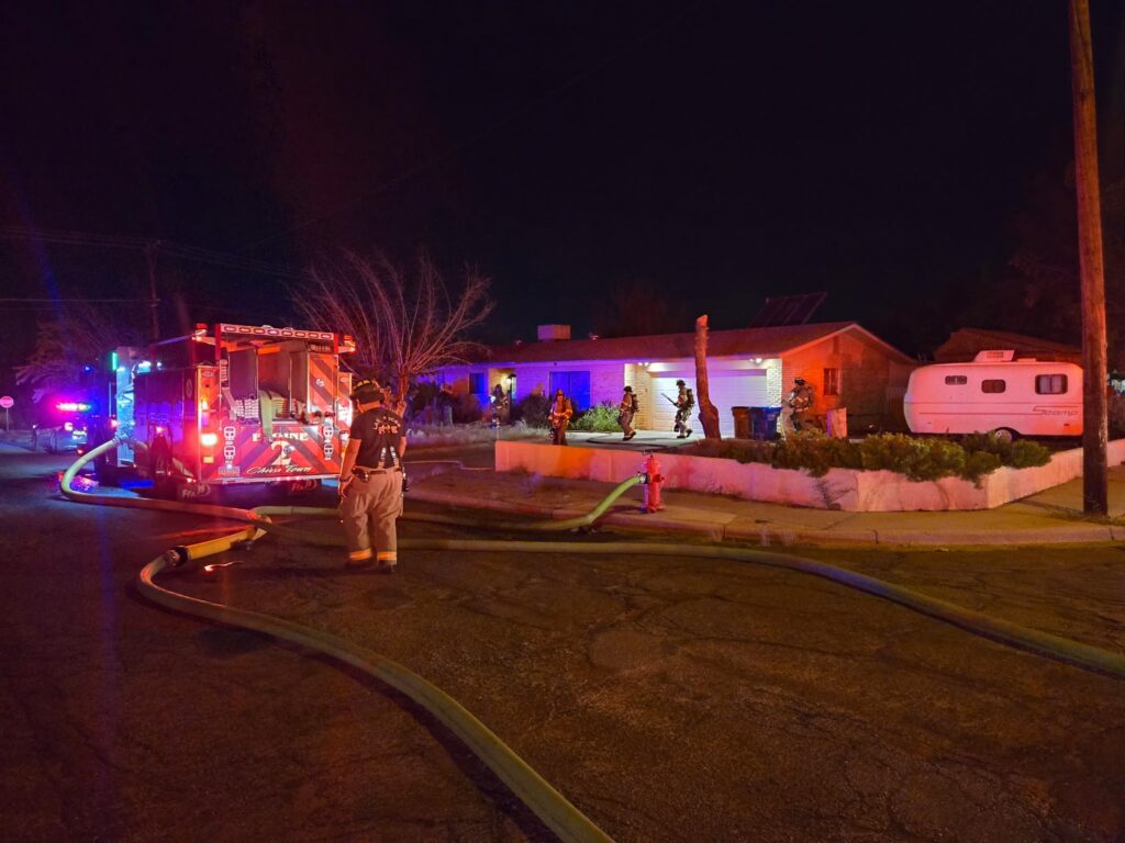 Firefighters standing outside of a house with a firetruck parked in the road.