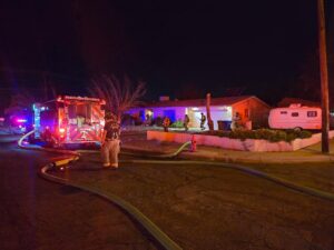 Firefighters standing outside of a house with a firetruck parked in the road.