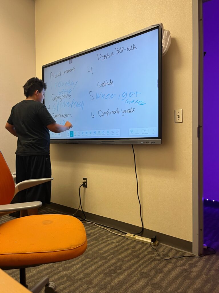 Young person writing on a large digital board with his finger.